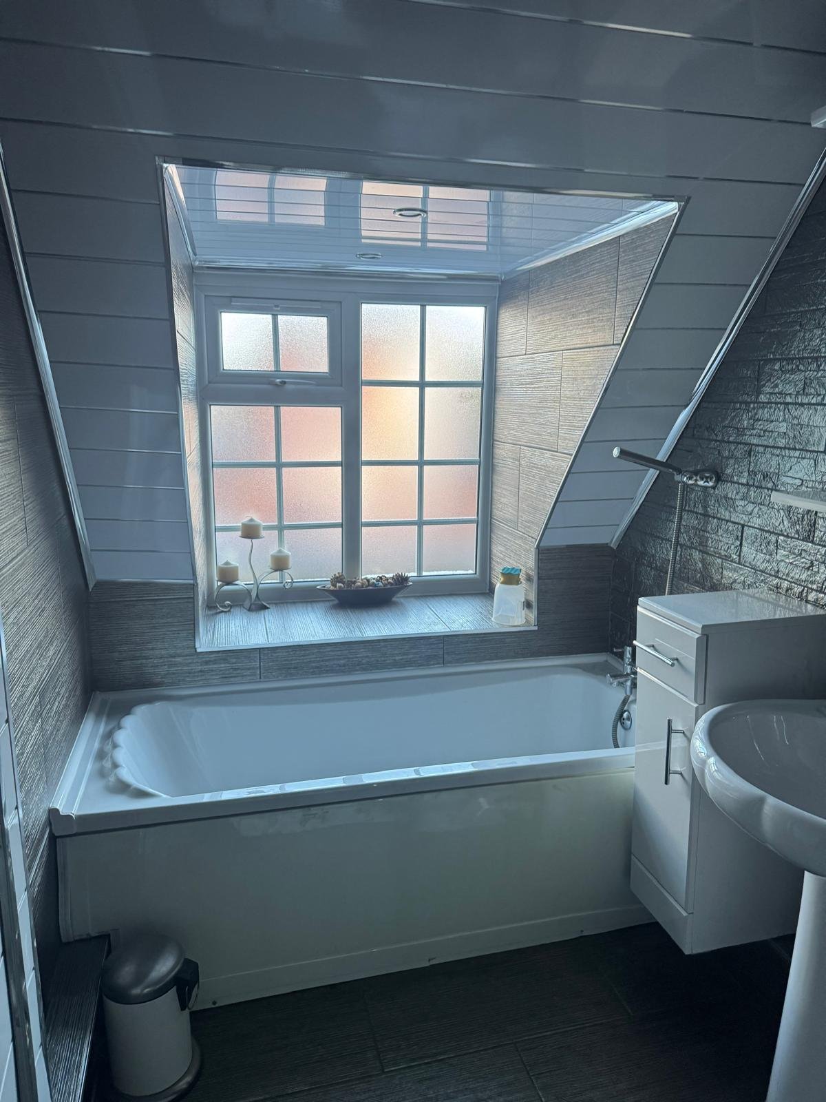 Modern bathroom with white bathtub, white toilet, and large window overlooking urban buildings with warm lighting