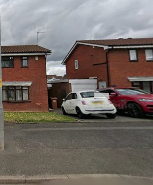 Red brick semi-detached houses with a white and red car parked in the driveway under an overcast sky