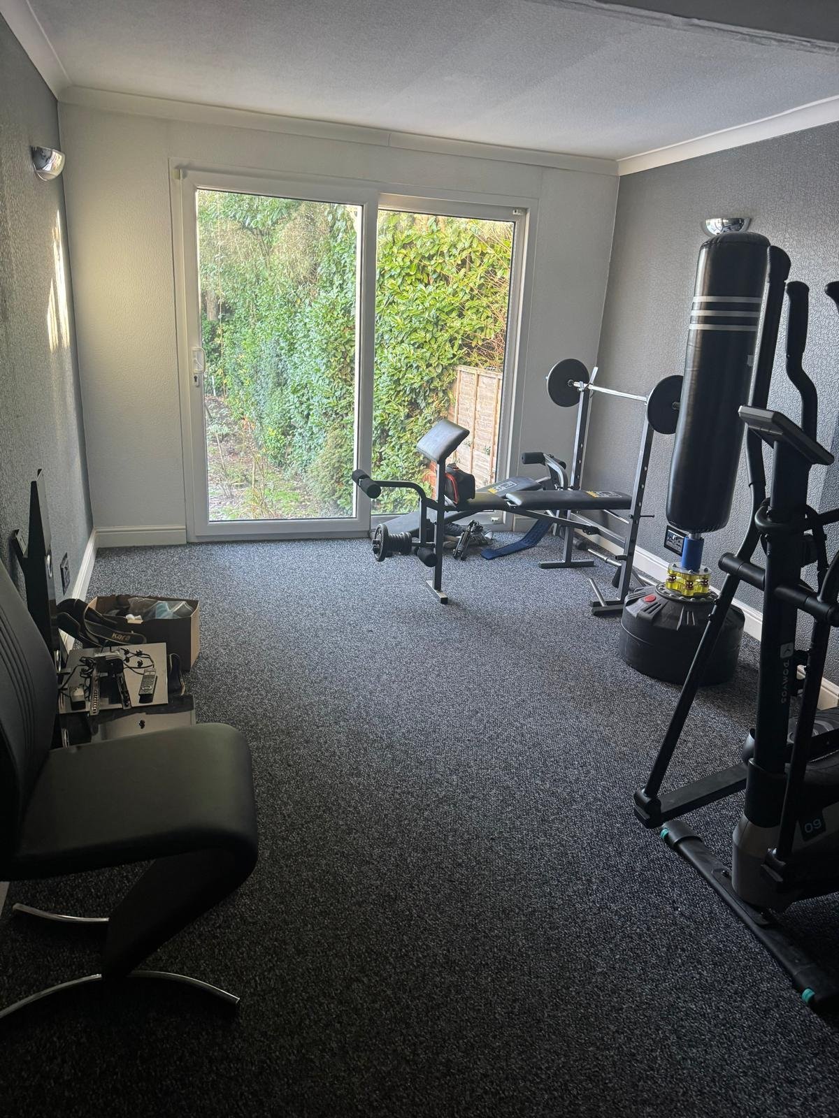 Home gym interior with exercise equipment including stationary bike and weight machines, glass doors overlooking green garden